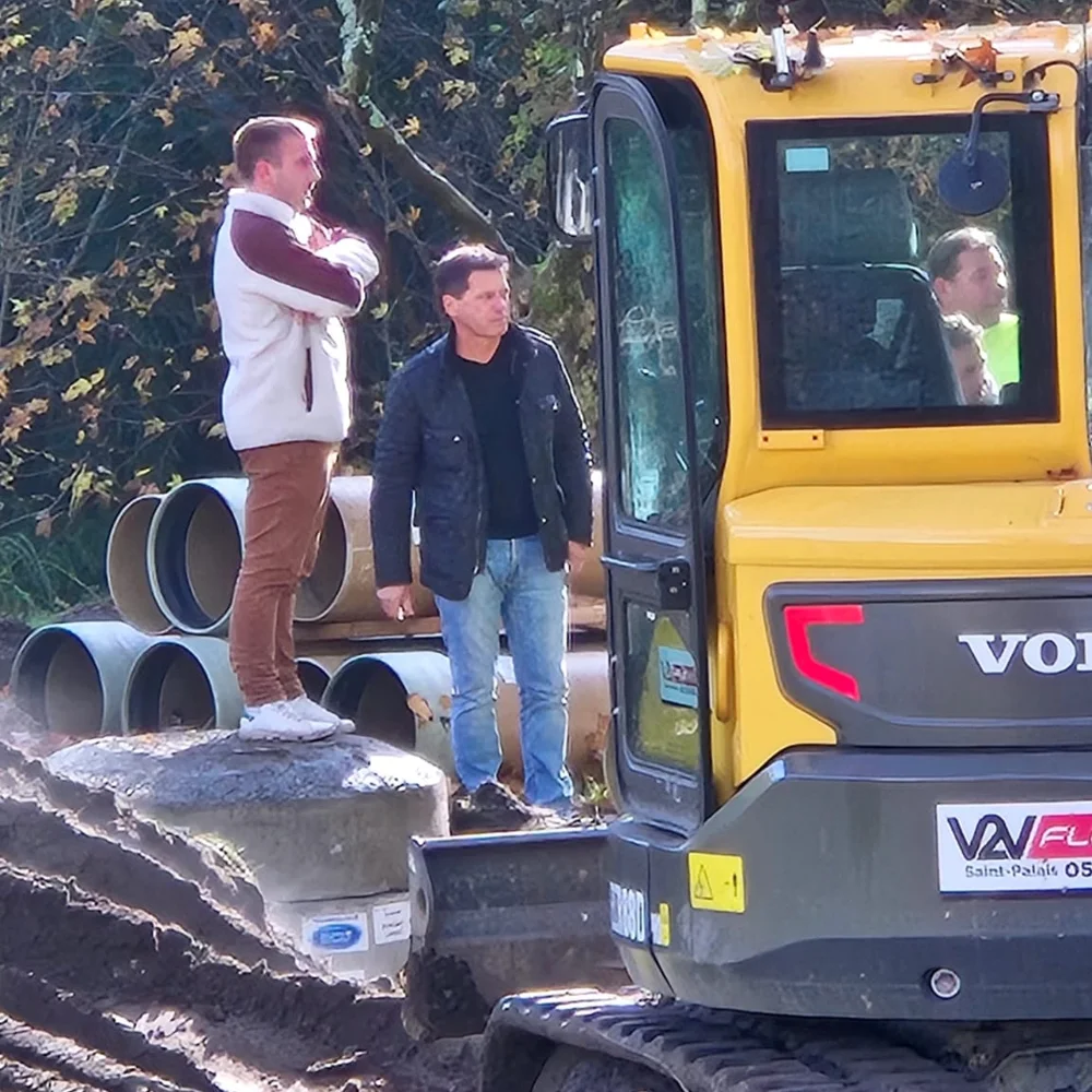 Suivi de chantier : deux personnes devant des tuyaux PRV stockés et une pelle mécanique