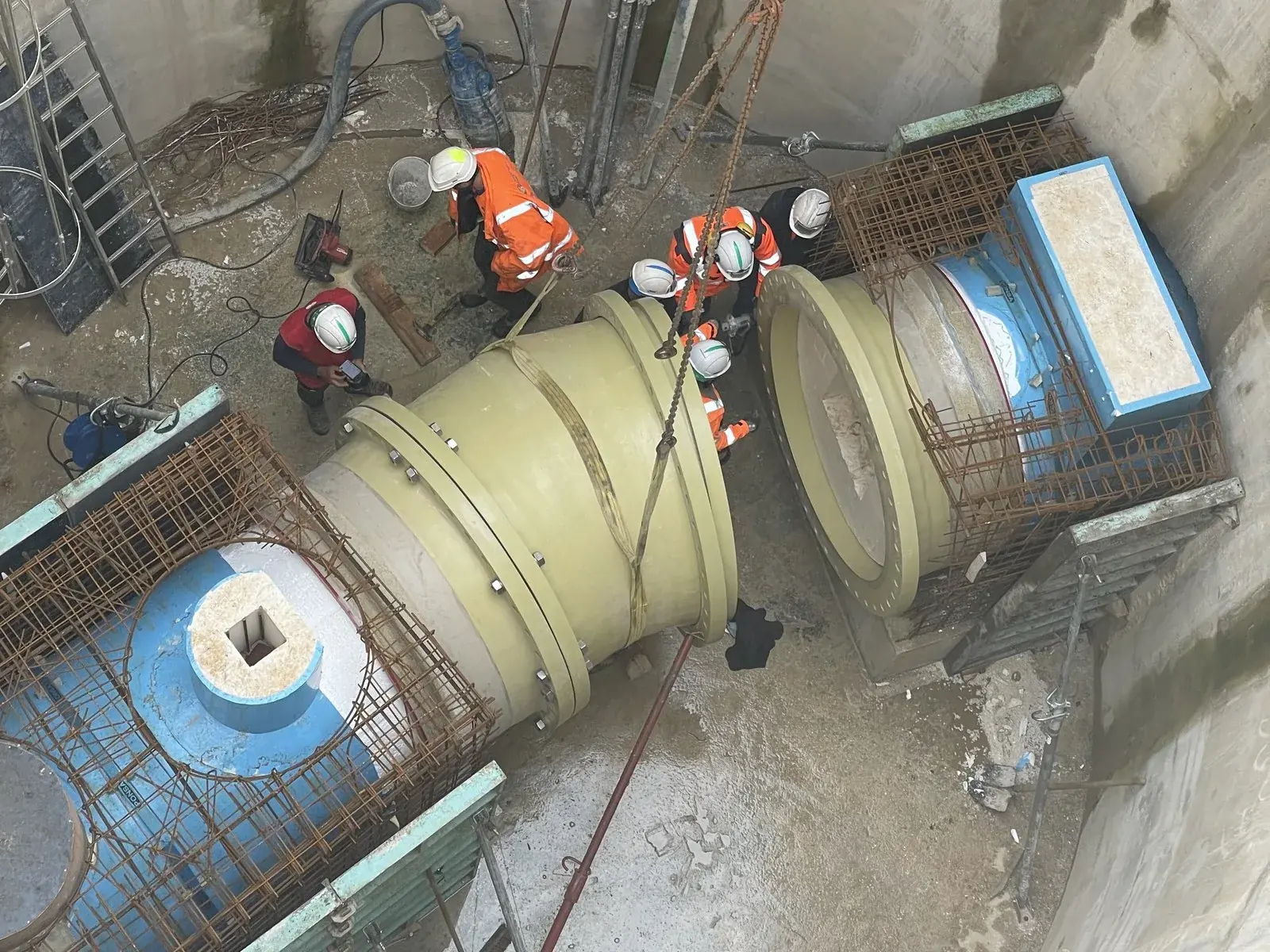 Installation crew at the bottom of a concrete shaft, GRP special fitting handled by a crane