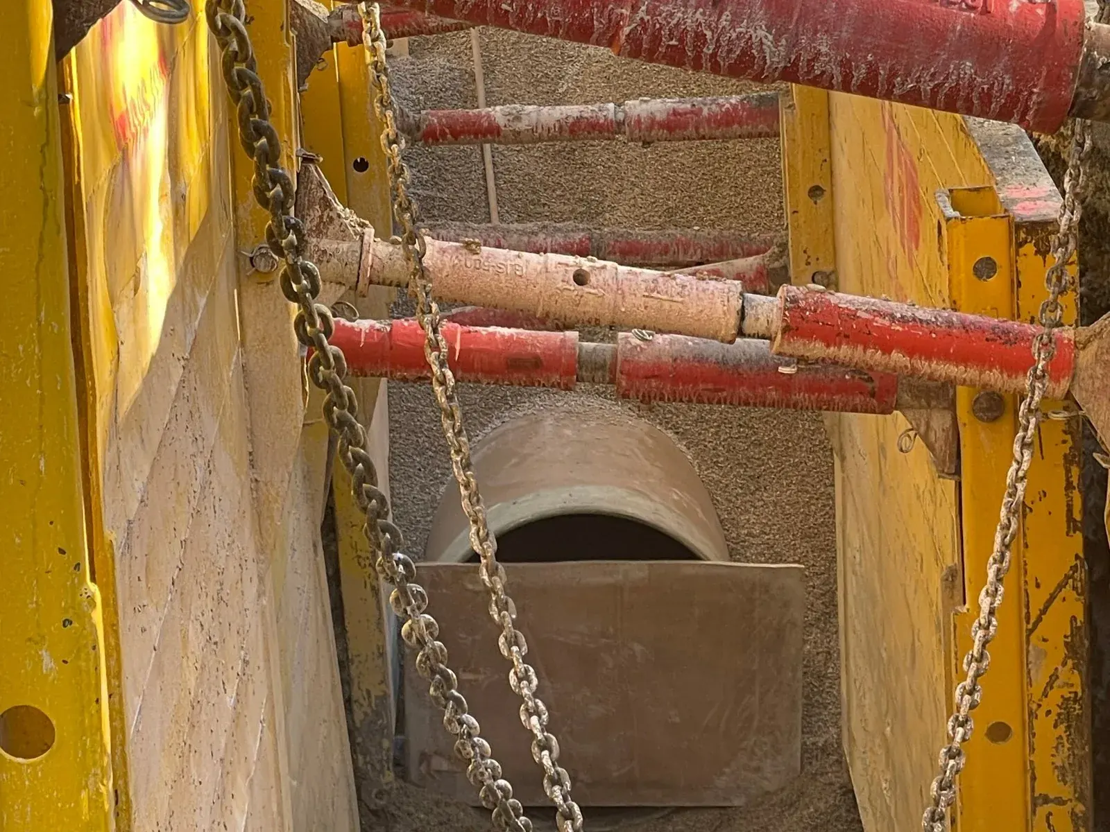 GRP pipe laid at the bottom of a shored trench, between red struts and yellow trench shields