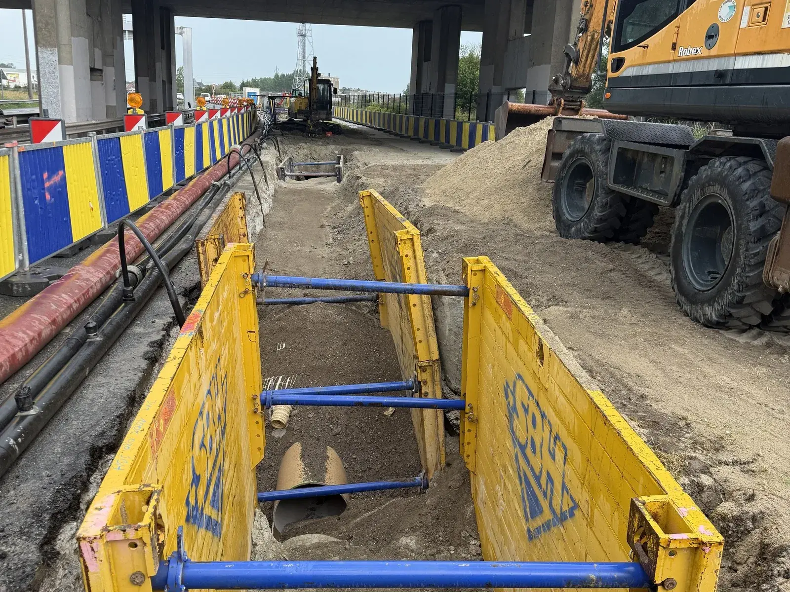 Tranchée blindée avec étais bleus sous un pont routier, canalisation en fond de fouille