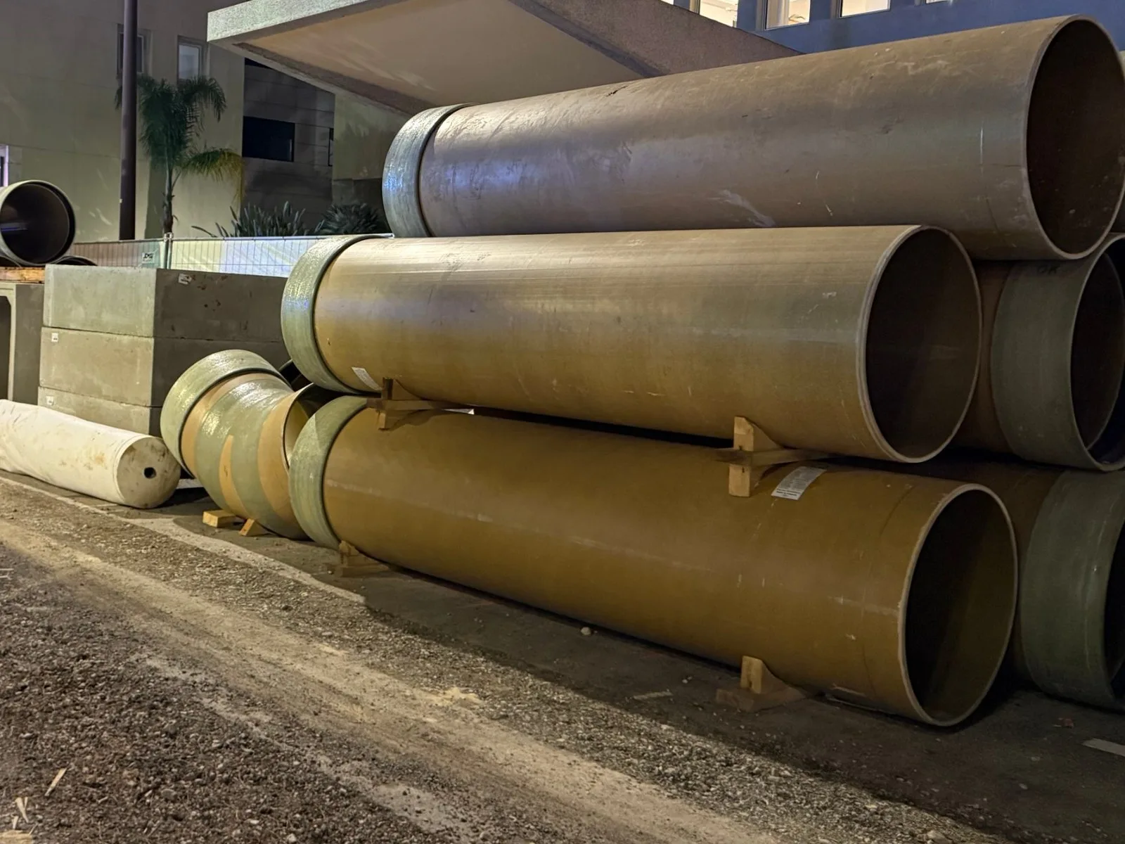 Tuyaux PRV et pièces de raccordement stockés le long d’un chantier urbain de nuit